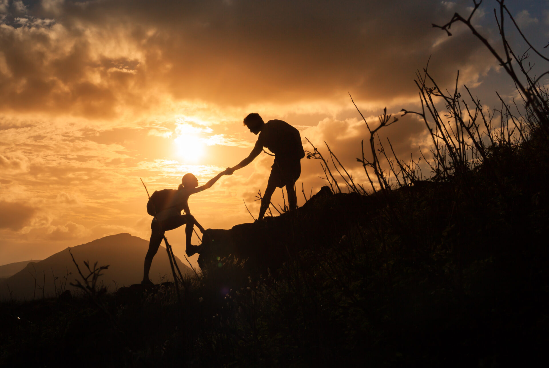 People helping each other hike up a mountain at sunrise.